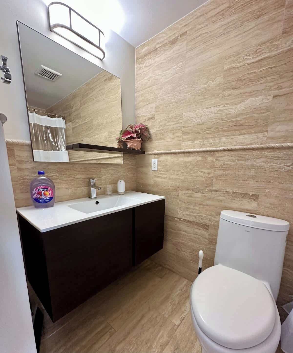 Ein Badezimmer mit einem weißen Waschbecken, dunklen Schränken, einer Toilette und einem Spiegel über dem Waschbecken.