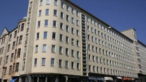 A multi-story building with a uniform facade, numerous windows, and a ground-level entrance with signage. - 2ndhomes Bright 1BR Home in Kamppi (Helsinki)