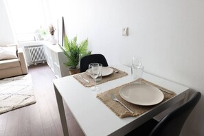 A dining table set with plates, glasses, and a fork, with a plant and a radiator in the background. - 2ndhomes Bright 1BR Home in Kamppi (Helsinki)