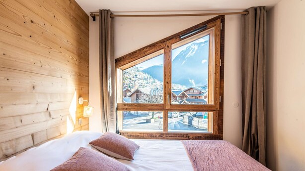 Ein Schlafzimmer mit großem Fenster, Holzwänden, einem Bett mit weißen Leinen und zwei Kissen.