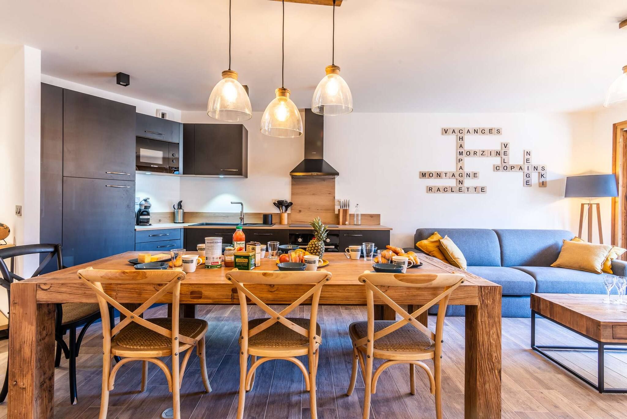 A modern kitchen with a wooden dining table, chairs, and pendant lights.