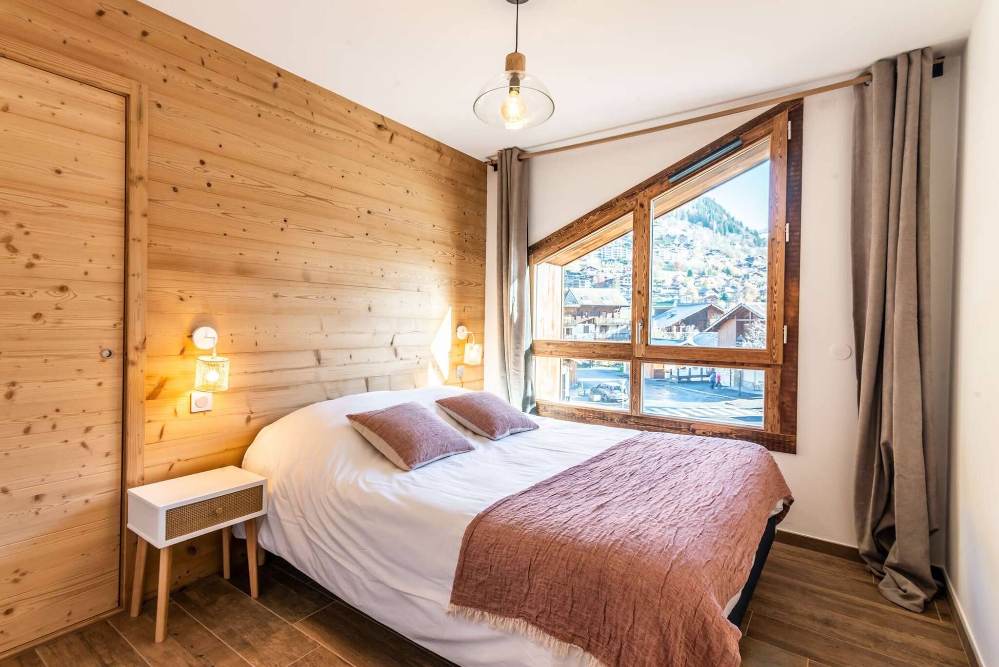 A wooden-paneled room with a bed, bedside lamps, and a window with a view of a snowy landscape.