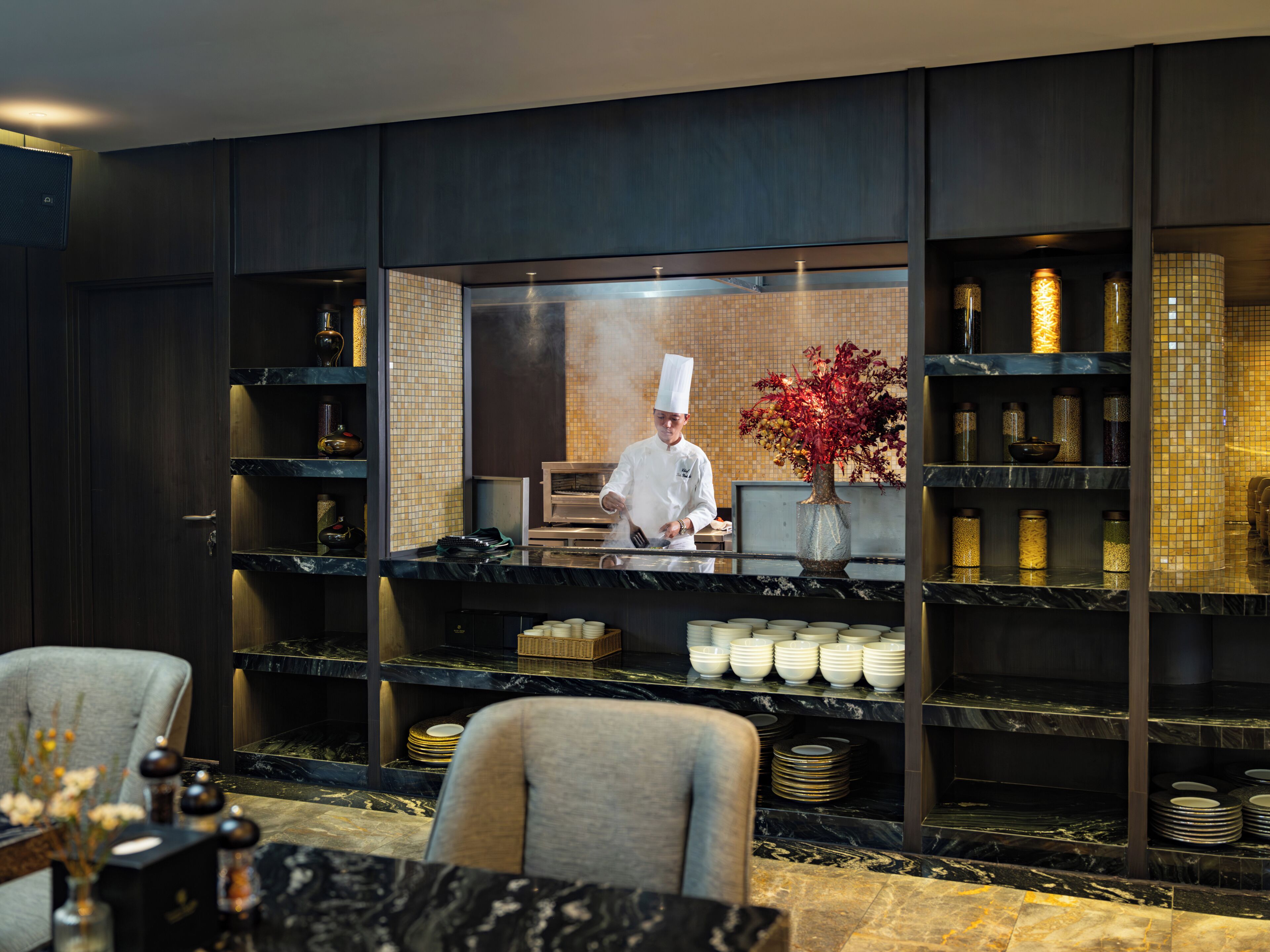 A chef preparing food in a modern kitchen with marble countertops and a tiled backsplash.