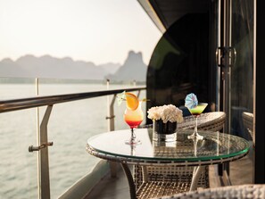 A glass table with drinks and flowers on a balcony overlooking water. - M'Gloria Cruise (Ha Long)