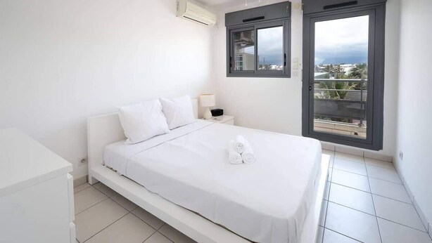 A bedroom with a bed, a nightstand, a window, and a view of the outside.