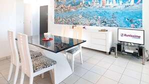 A modern dining area with a glass table, white chairs, a ceiling fan, and a large space-themed mural on the wall.