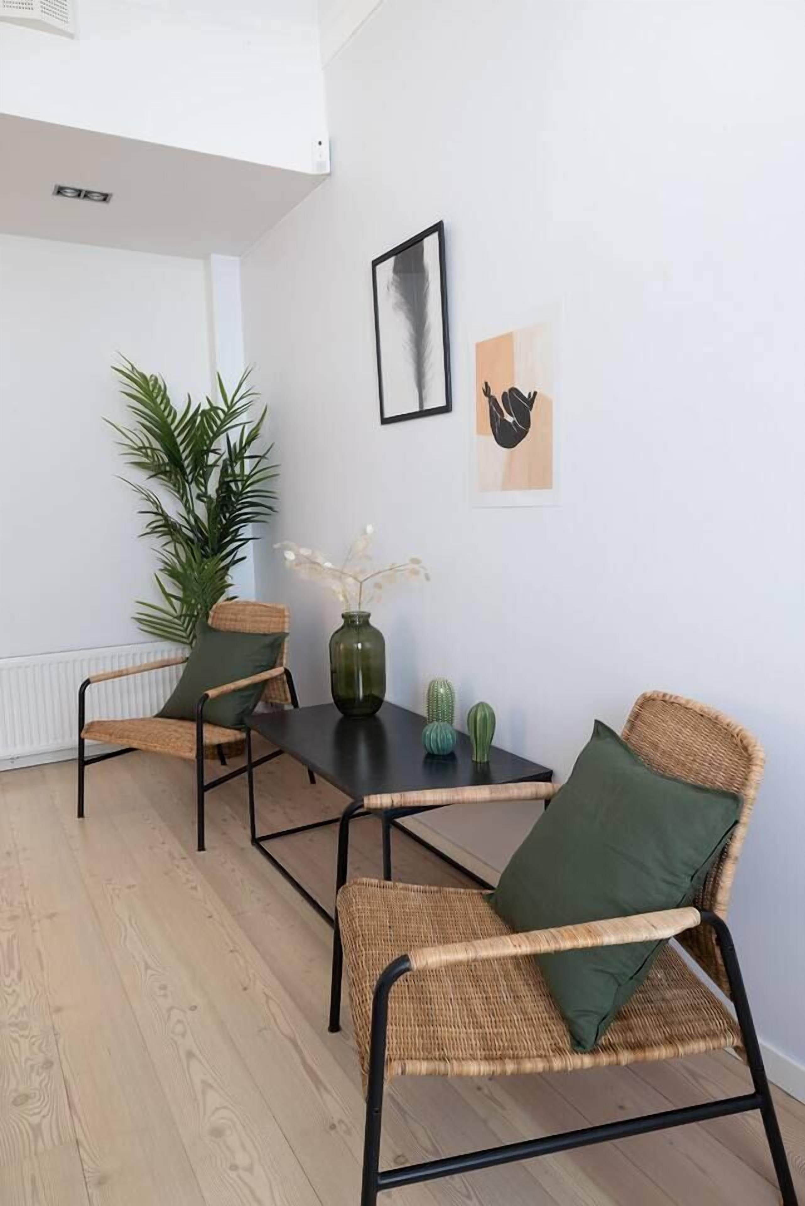 A dining area with wicker chairs, a black table, a green vase, and a potted plant.