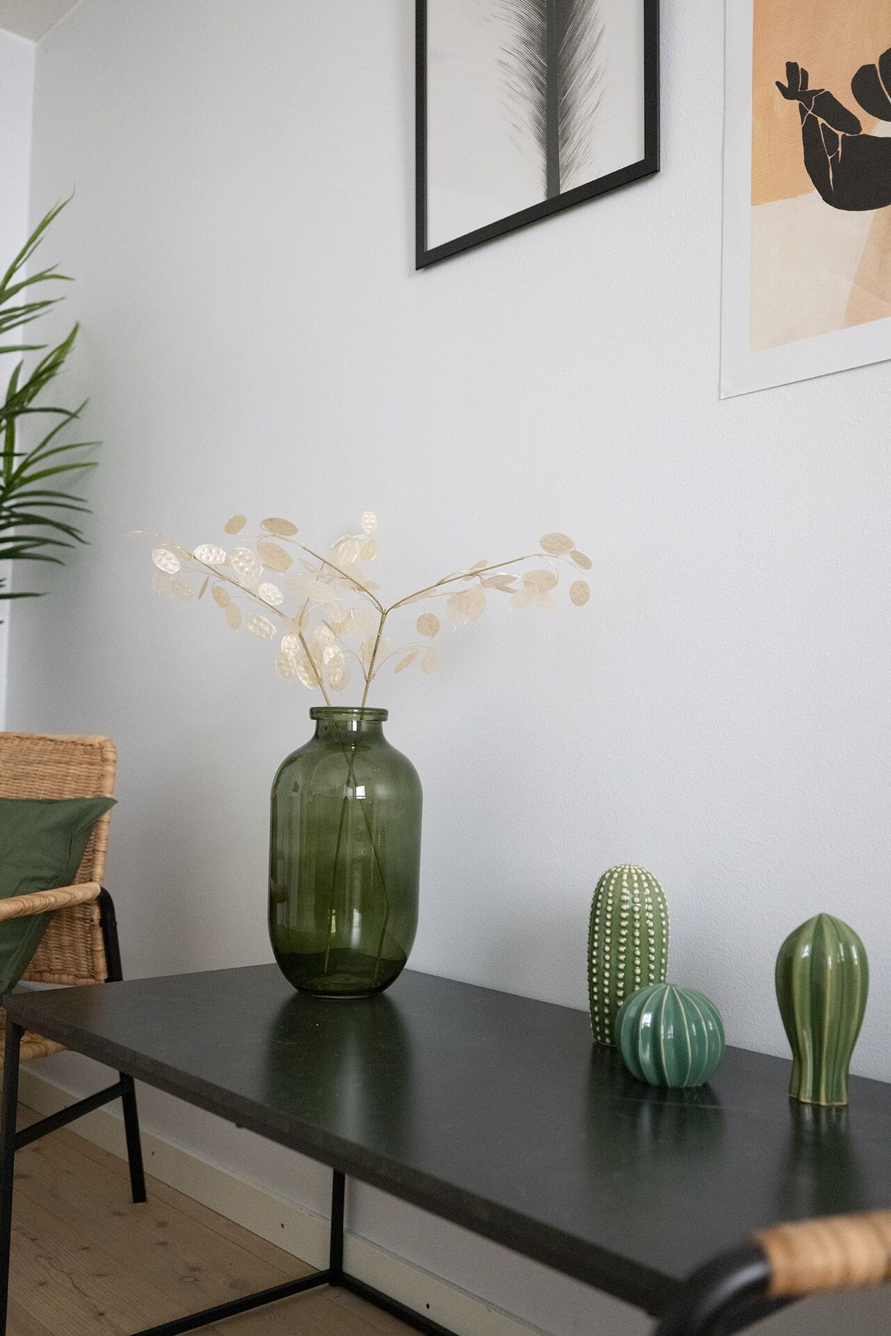 Una stanza con un tavolo in legno scuro, un vaso verde con fiori secchi e due vasi decorati con motivi verdi.