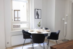A dining area with a round table, black chairs, and a window with blinds.