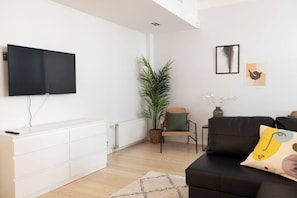 A modern living room with a flat-screen TV, a sofa, a chair, a potted plant, and artwork on the wall.
