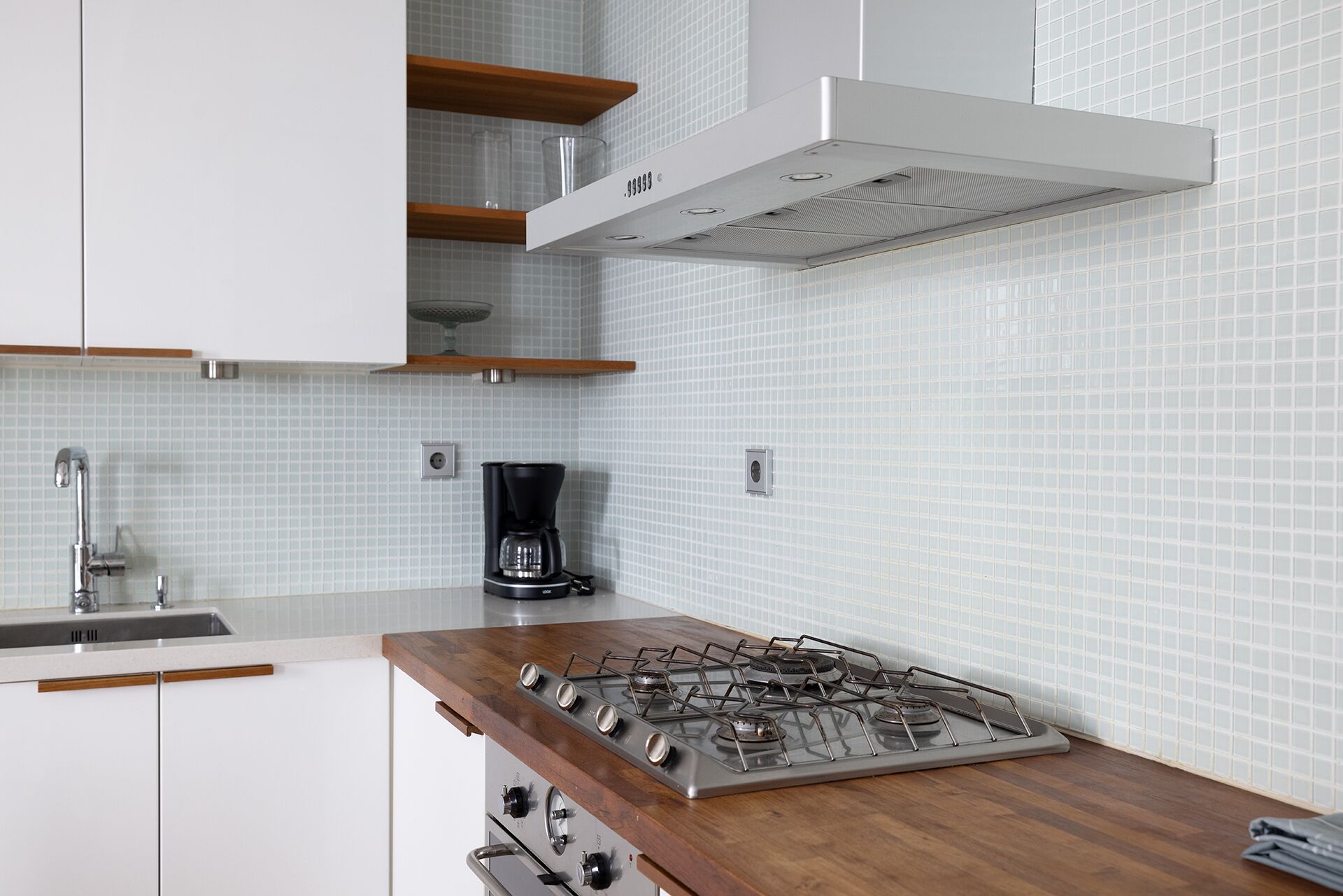 A modern kitchen with white cabinets, a stainless steel stove, and a coffee maker on the counter.