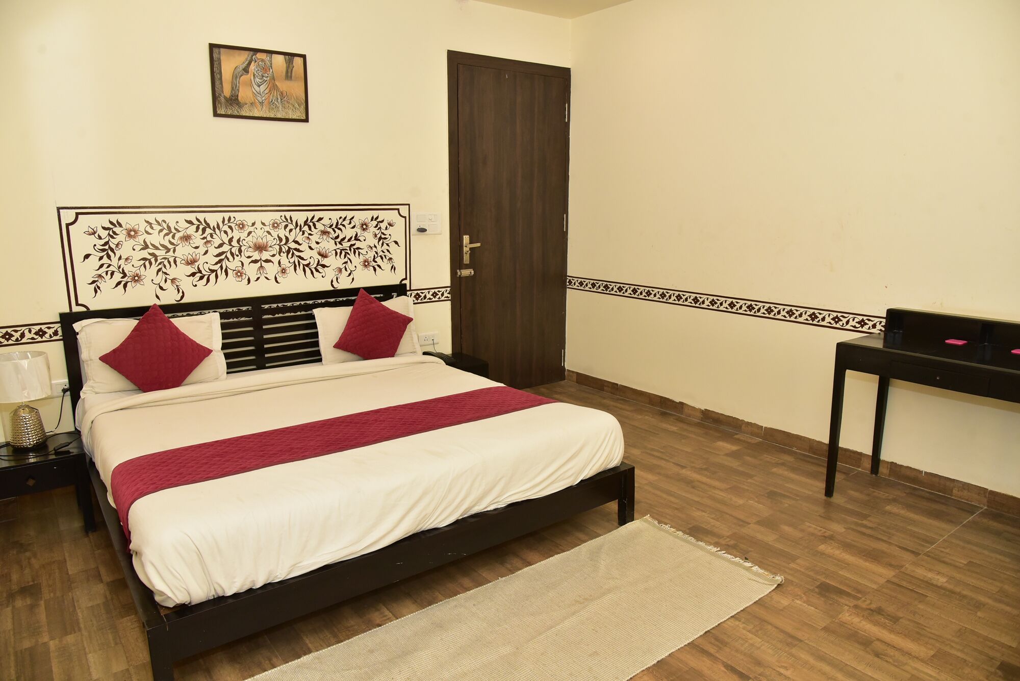 A bedroom with a bed, a nightstand, a desk, a door, and a wall with a floral pattern.