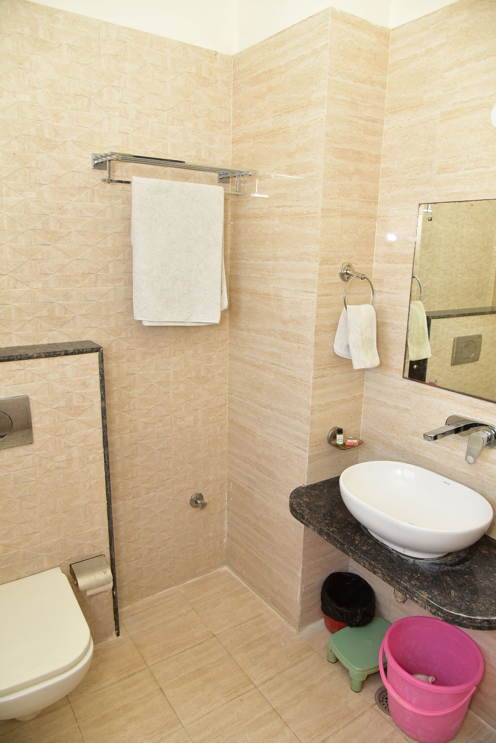 A bathroom with a toilet, sink, mirror, towel rack, and a small trash bin.