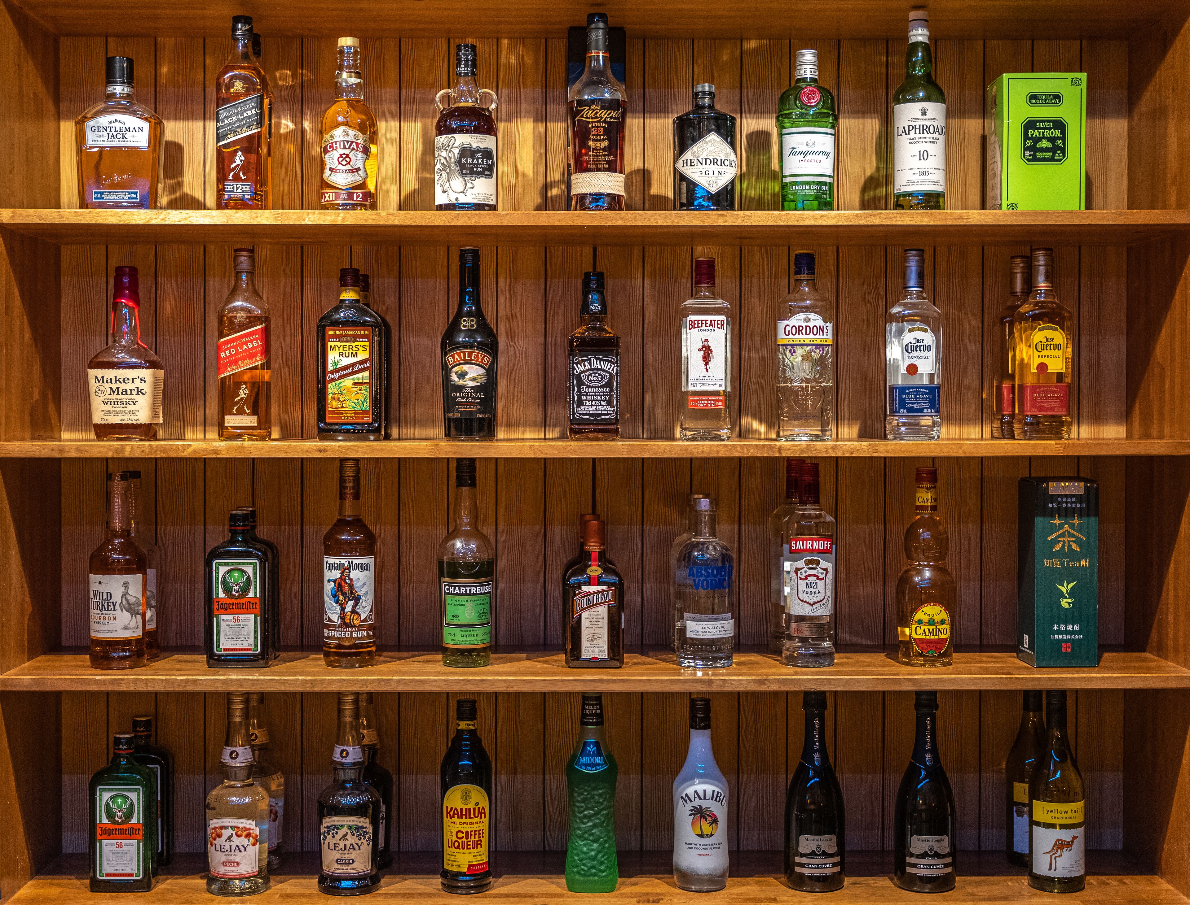 A wooden shelf with various bottles of alcohol, including whiskey, gin, and liqueurs.