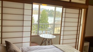 A room with a bed, a small round table, and a view of a lake through large windows. - Elan Hotel Lake Nojiri (Shinano)