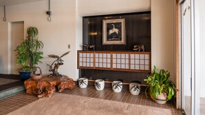 A reception area with a wooden reception desk, a large potted plant, a framed artwork, and a traditional Japanese screen. - Elan Hotel Lake Nojiri (Shinano)