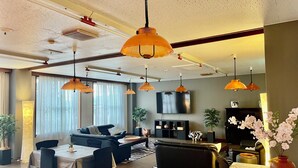 A modern living room with a sofa, dining table, and chairs, a flat-screen TV mounted on the wall, and multiple pendant lights. - Elan Hotel Lake Nojiri (Shinano)