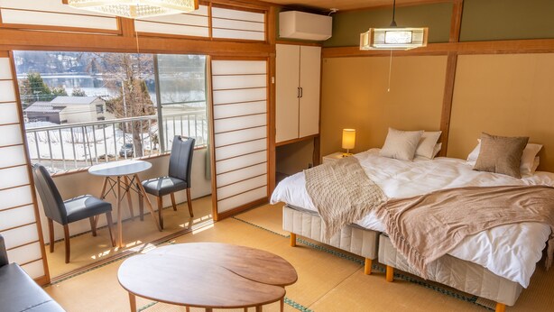 A hotel room with tatami flooring, a bed, a small round table, and a balcony with chairs. - Elan Hotel Lake Nojiri (Shinano)