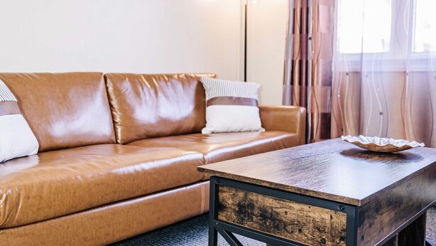 Una sala moderna con un sofá de cuero marrón, una mesa de centro de madera y una lámpara de pie.