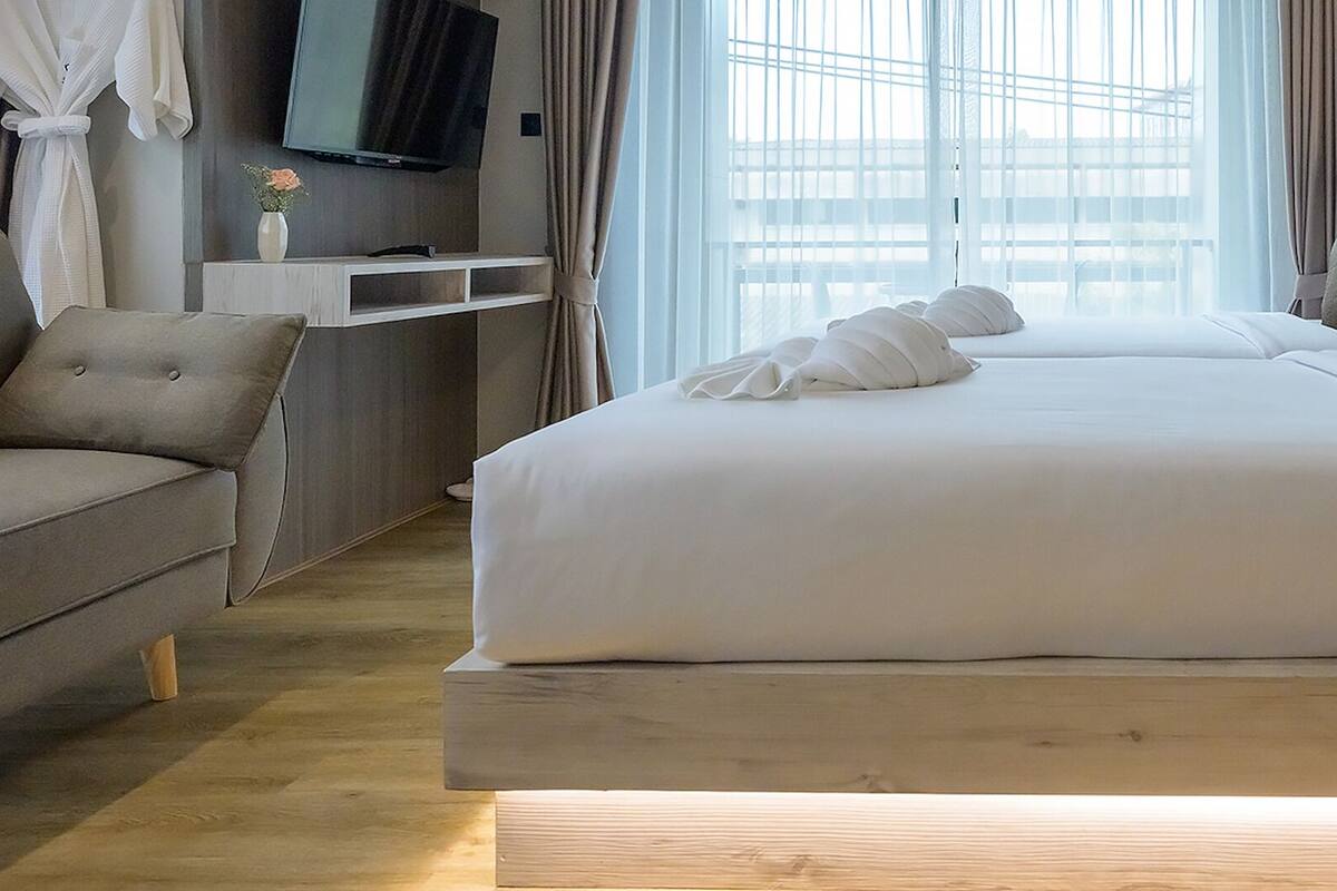 A modern hotel room with a large bed, a sofa, a bedside table, and a TV mounted on the wall.