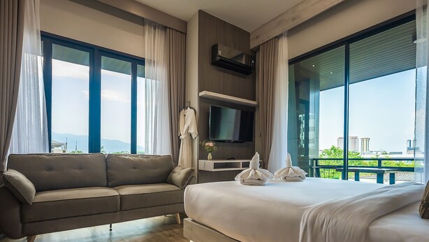 A modern hotel room with a large bed, a sofa, a TV, and a balcony with a city view. - Le Bis Hotel  (Chiang Mai)