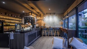 A modern cafe with a bar area, seating, and large windows. - Le Bis Hotel  (Chiang Mai)