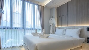 A modern hotel room with a large bed, a bedside table with a phone, and a view of the outdoors through sheer curtains. - Le Bis Hotel  (Chiang Mai)