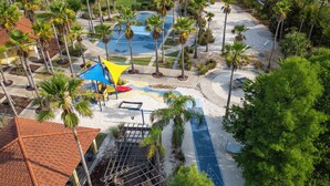 Oversigtsbillede af et resort med poolområde, palmer og en legeplads.