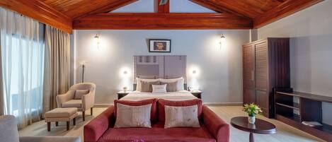 A bedroom with a wooden ceiling, a bed with a headboard, bedside lamps, a TV, and a fireplace.