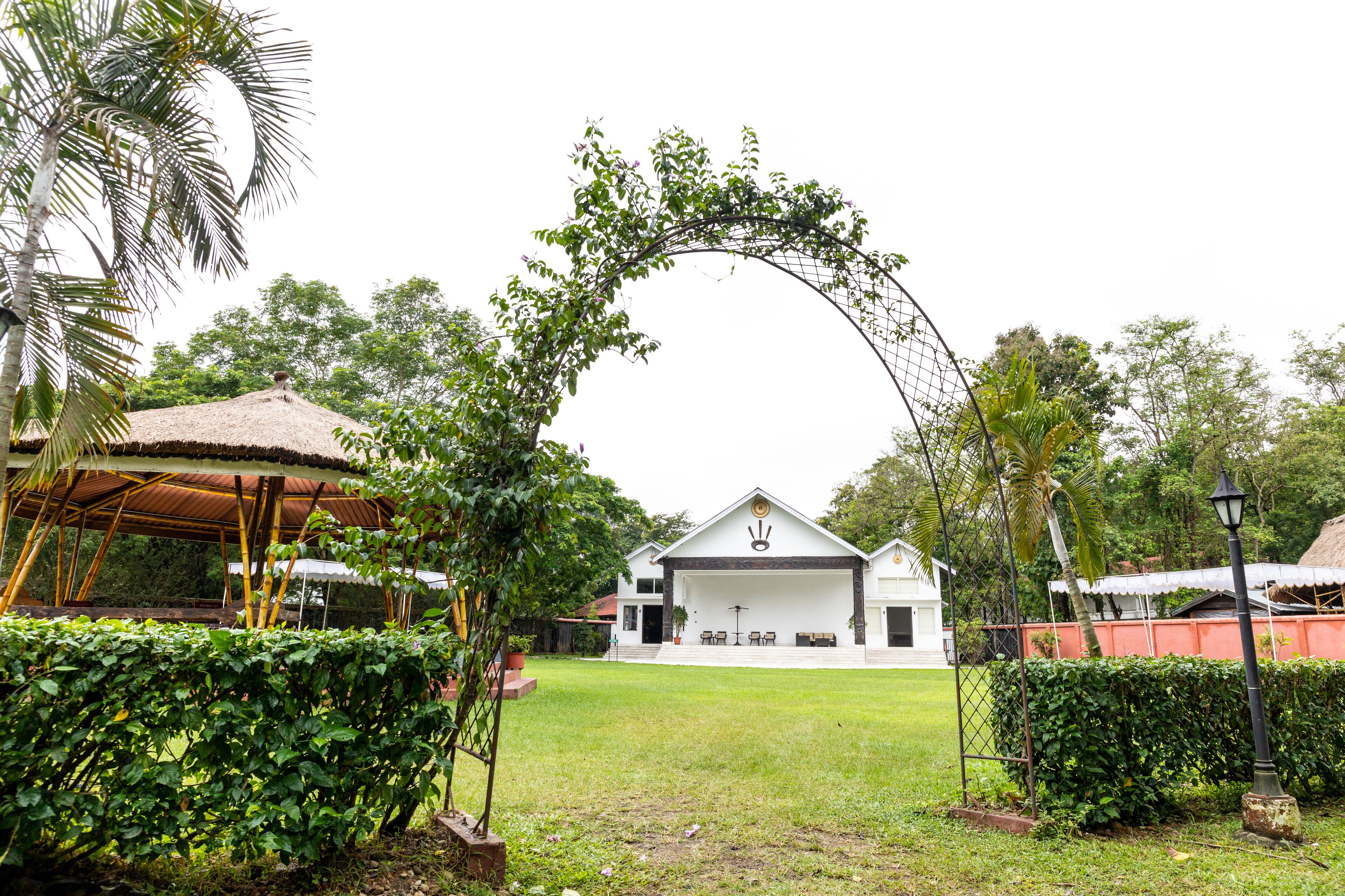 A white building with a thatched roof, surrounded by lush greenery and a decorative archway.