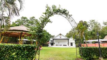 A white building with a thatched roof, surrounded by lush greenery and a decorative archway.