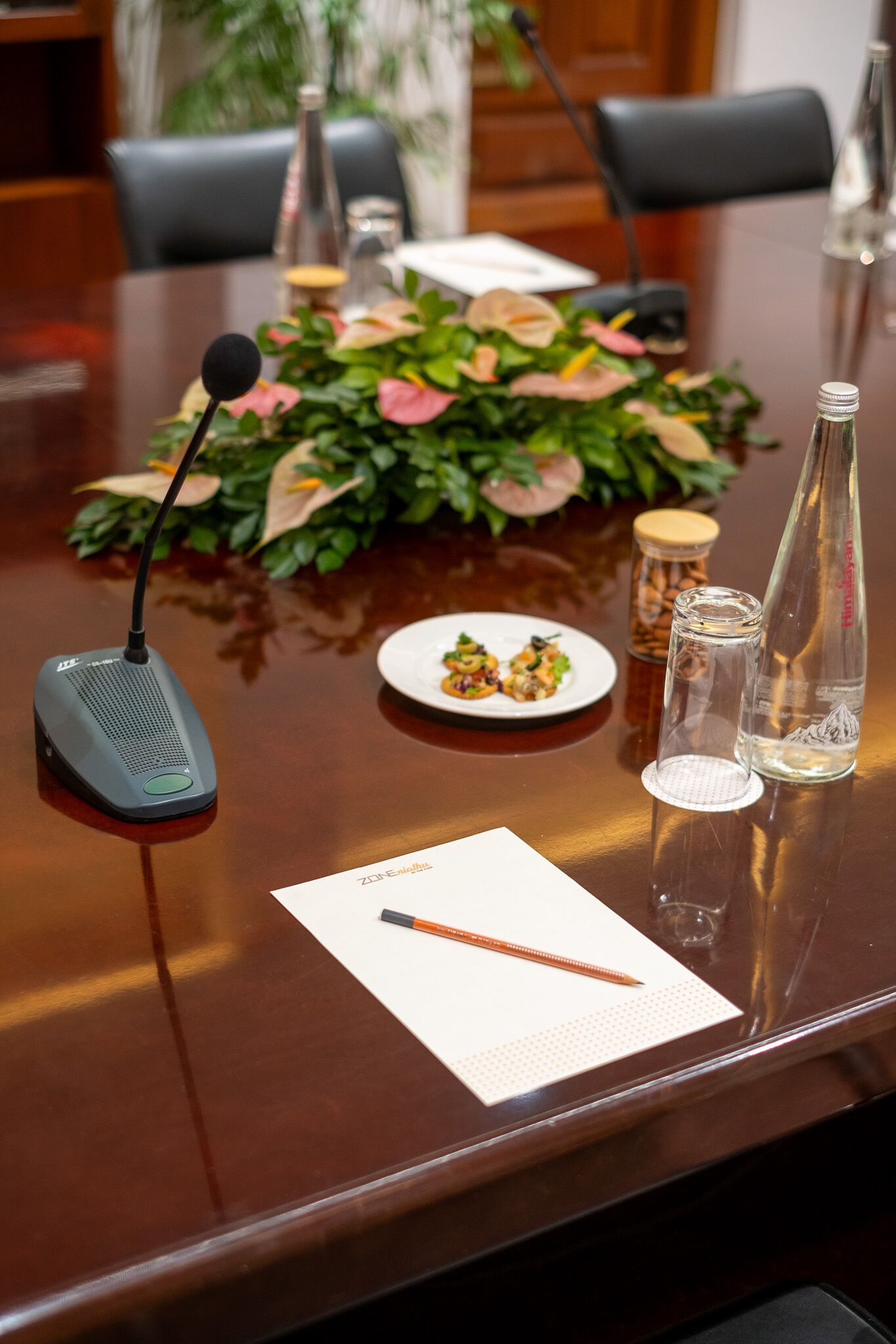 Une table de conférence avec un microphone, une assiette de nourriture, deux bouteilles et un bloc-notes.