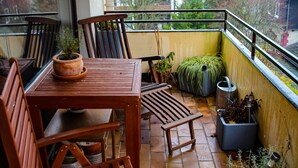 A balcony with a wooden table and chairs, potted plants, and a view of houses and trees.