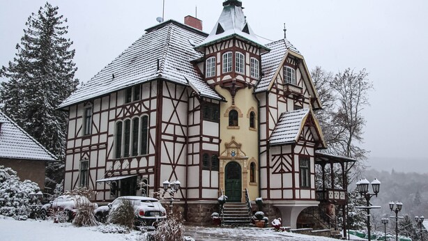 A traditional half-timbered house with a steeply pitched roof, a central tower, and a green door.