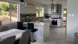 Een moderne keuken met een centraal eiland, grote ramen en een zithoek met barstoelen.