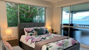 Een slaapkamer met een groot bed, een stoel en uitzicht op de zee door een schuifdeur.