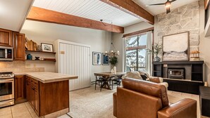 A kitchen with wooden cabinets, a built-in microwave, and a large island. There is a dining area with a table and chairs, and a living room with a leather sofa and a fireplace.