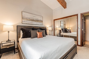 A bedroom with a large bed, two bedside tables, a nightstand, a mirror, and a painting on the wall.