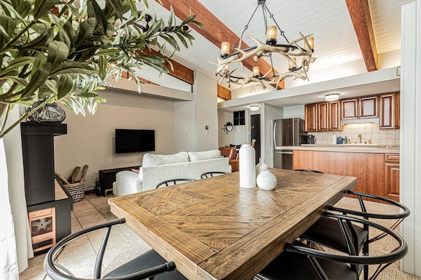 A modern kitchen with wooden cabinets, a dining table with chairs, and a hanging light fixture.