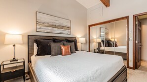 A bedroom with a large bed, two bedside tables, a mirror, and a ceiling with exposed beams.