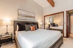 A bedroom with a large bed, two bedside tables, a mirror, and a ceiling with exposed beams.