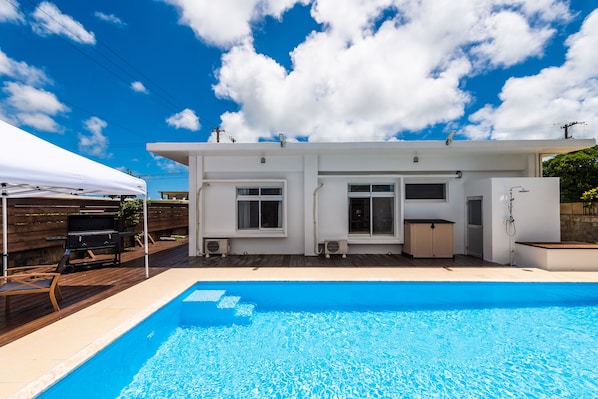 Enjoy a refreshing swim in the pool surrounded by a covered outdoor area with a barbecue grill and seating.