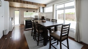A modern kitchen with a wooden ceiling, a dining table with chairs, and large windows with curtains. - MARINUS (Miyakojima)
