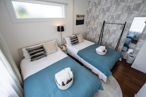 Two single beds with teal bedspreads and white pillows, a wicker basket, and a framed picture adorn this cozy retreat.