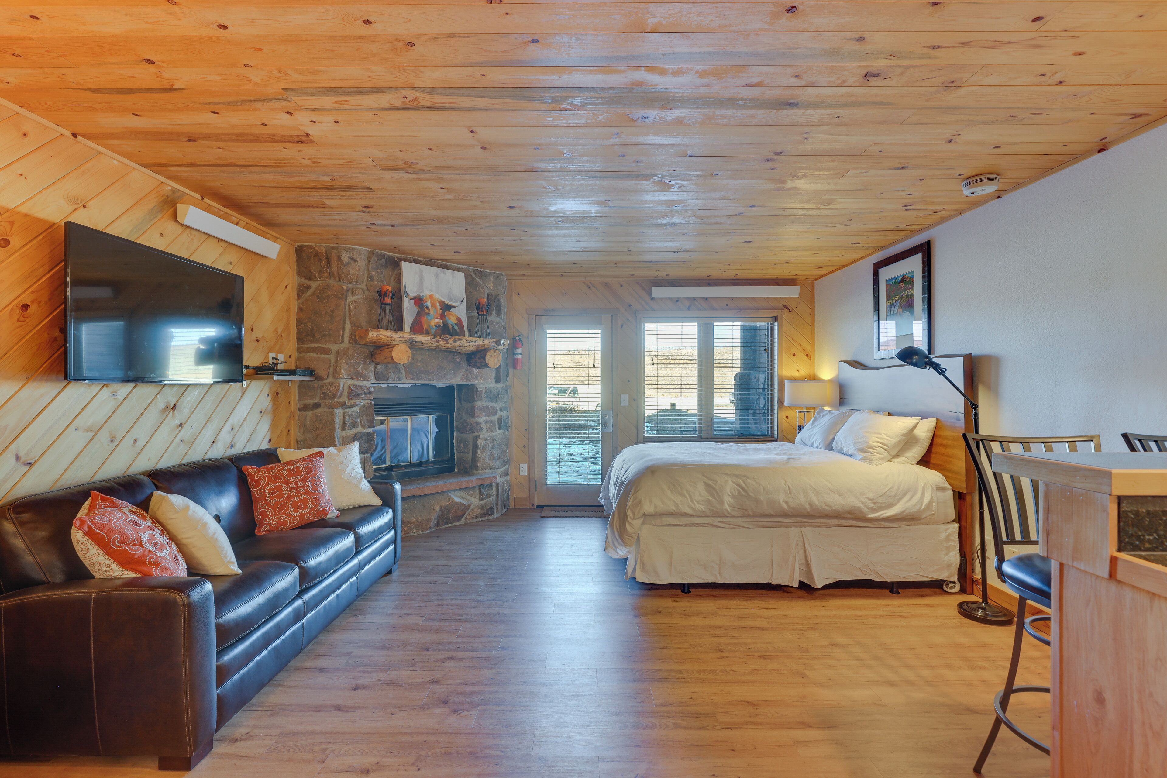 A cozy room with a stone fireplace, a large bed, a leather sofa, and a television mounted on the wall.