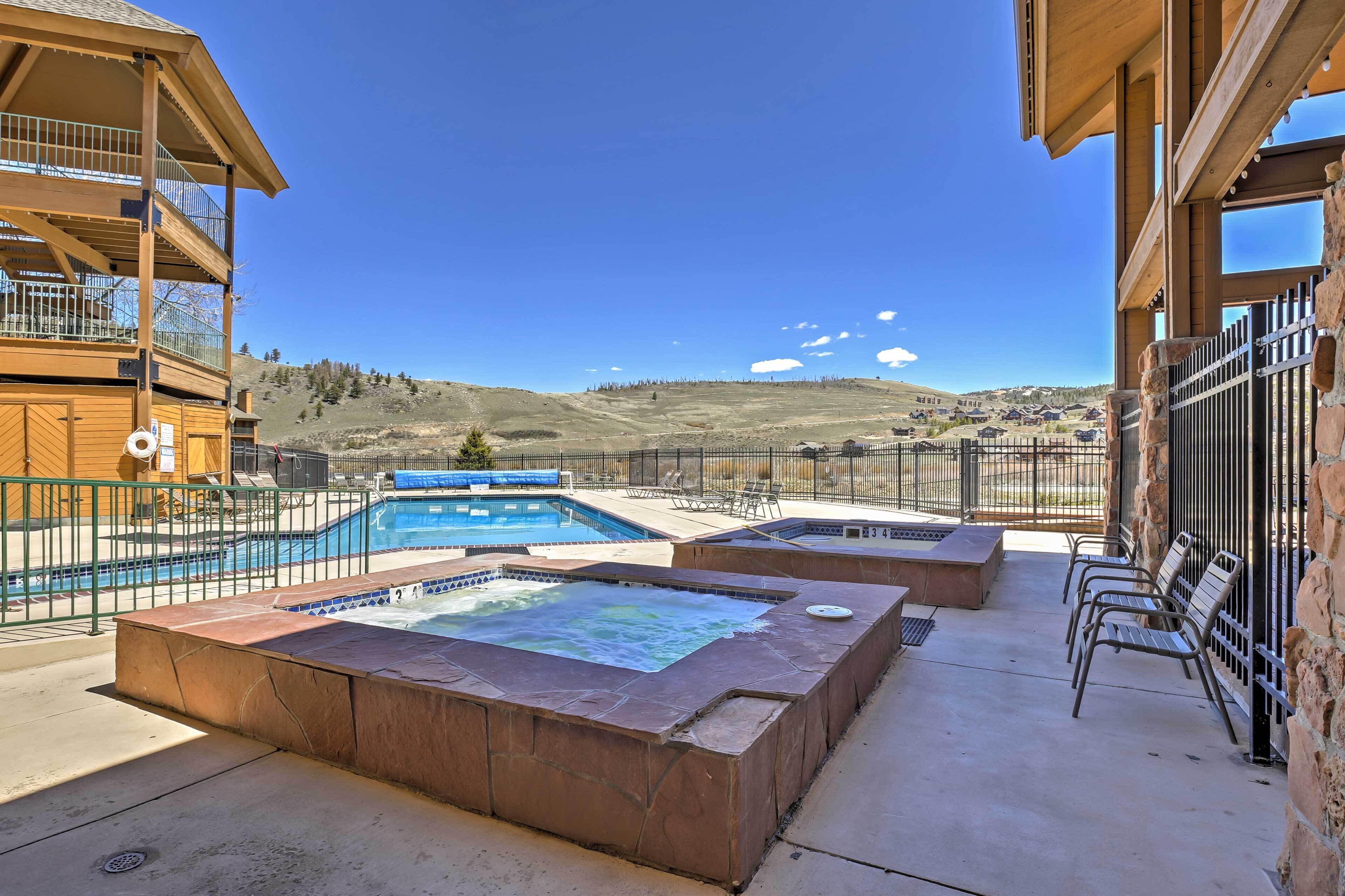 A pool area with a hot tub, outdoor seating, and a view of a mountainous landscape.