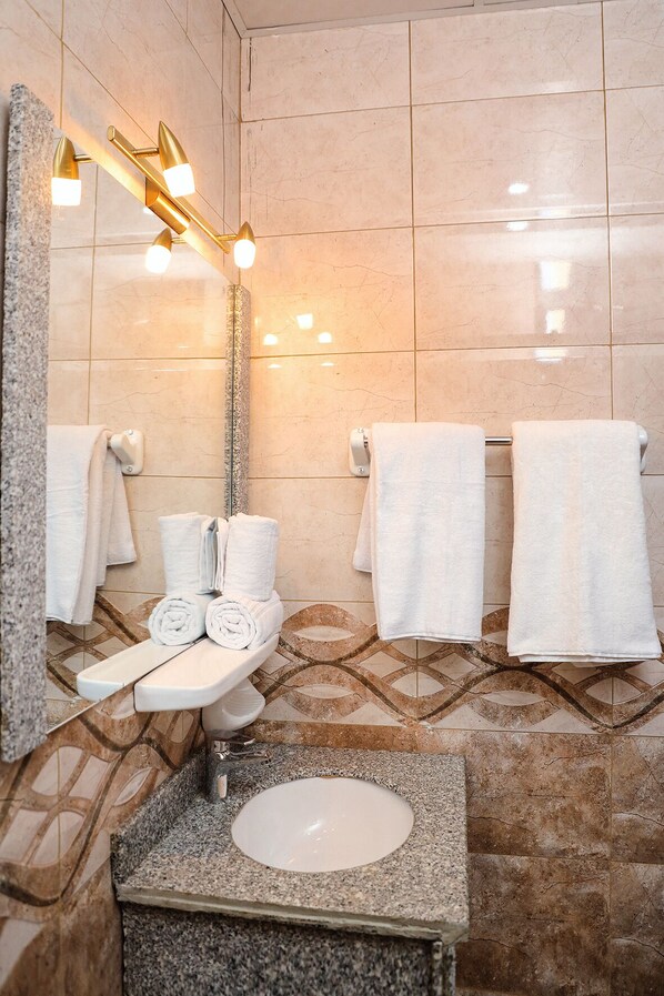 A bathroom with a granite sink, a mirror with lights, and multiple white towels. - South Gate Hotel Apartment (Addis Ababa)