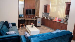 A compact living space with a sofa, a coffee table, a TV, and a kitchenette. - South Gate Hotel Apartment (Addis Ababa)