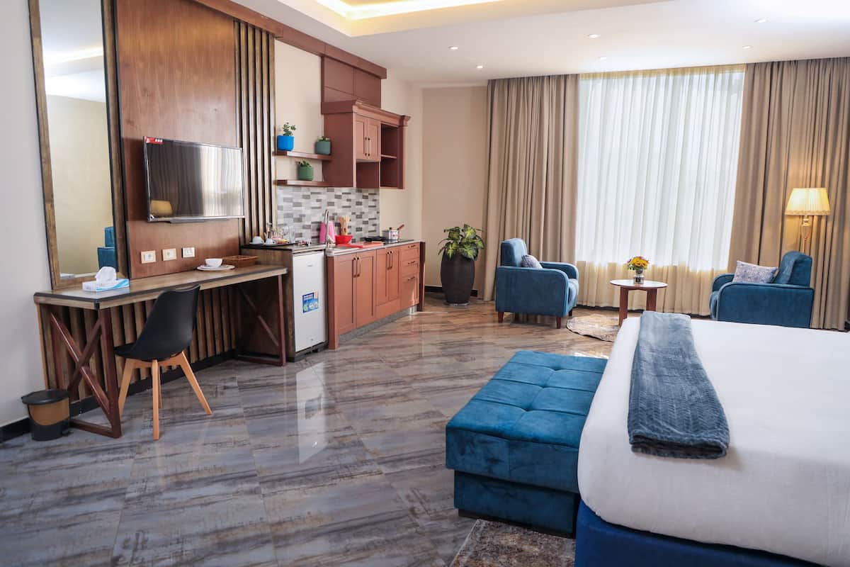 Une chambre d’hôtel comprenant un lit, un bureau avec une chaise, un canapé, une petite table avec une lampe et une grande fenêtre avec des rideaux.