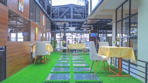 An indoor dining area with artificial grass flooring, tables with yellow checkered tablecloths, and chairs with wooden legs. - South Gate Hotel Apartment (Addis Ababa)